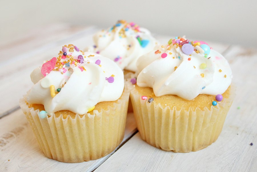 Vanilla cupcakes topped with white frosting and colourful sprinkles
